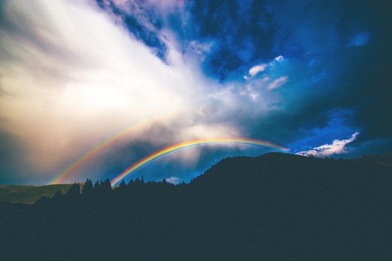 Foto de um arco-íris sobre as montanhas no crepúsculo por Abigail Keenan no Unsplash
