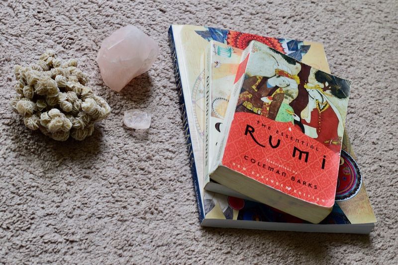 Купчина от три книги, The Essential Rumi, Guided by the Moon и The Shaman’s Guide to Power Animals, върху бял килим, до розов кварц, кула и чип и розов селенит от